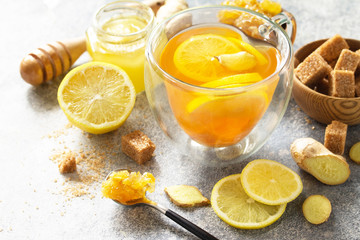 Hot cup of ginger tea and ingredients - lemon, ginger, honeycomb, honey on a gray stone countertop.