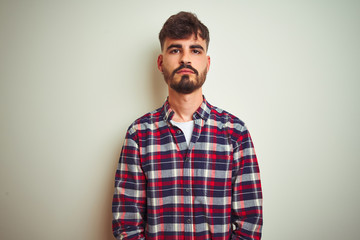 Obraz premium Young man wearing casual shirt standing over isolated white background with serious expression on face. Simple and natural looking at the camera.