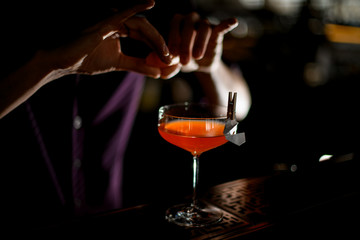 Male bartender spraying on the cocktail decorated with paper airplane in the clothespin with a orange zest juice