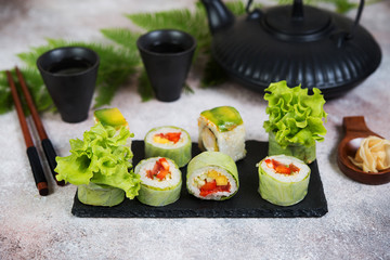Vegetable vegetarian sushi rolls with a teapot of tea and Chinese cups stand on a concrete table.