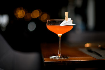 Orange alcoholic cocktail in the glass decorated with a paper airplane in the clothespin