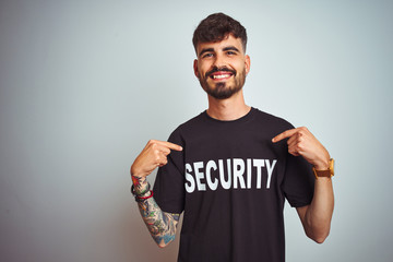 Young safeguard man with tattoo wering security uniform over isolated white background looking...
