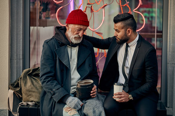 Rich man in tuxedo and homeless person in dirty clothes sitting and talking in the street. Poverty,...