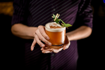 Barman serving a creamy color cocktail drink decorated with a green tropical leaf and black berry on the toothpick