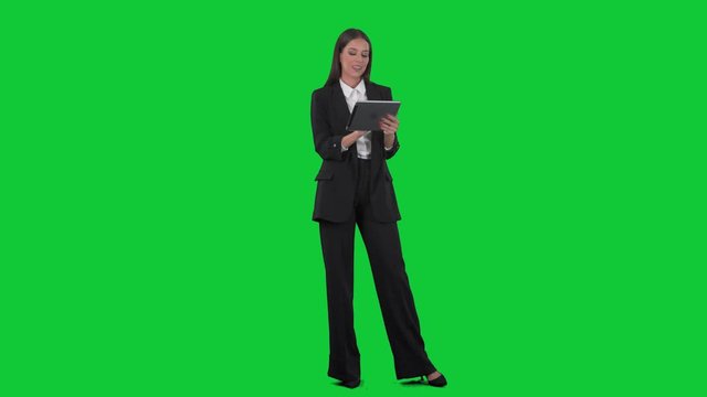 Young happy business woman in suit working on tablet using touch screen technology. Full length on green screen background. 