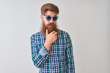 Young redhead irish man wearing casual shirt and sunglasses over isolated white background looking confident at the camera smiling with crossed arms and hand raised on chin. Thinking positive.