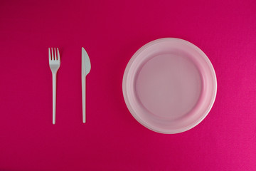 Disposable plastic plate, fork and knife on a pink background. Table setting