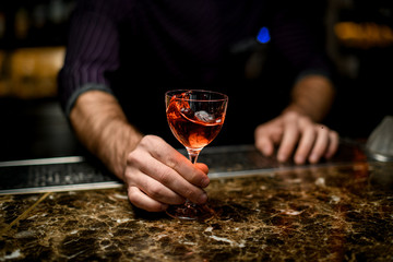 Professional male bartender serving an orange short cocktail in the little glass