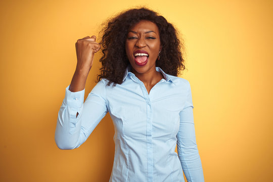 African american businesswoman wearing elegant shirt over isolated yellow background angry and mad raising fist frustrated and furious while shouting with anger. Rage and aggressive concept.