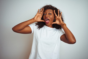 Young african american woman wearing t-shirt standing over isolated white background Smiling cheerful playing peek a boo with hands showing face. Surprised and exited