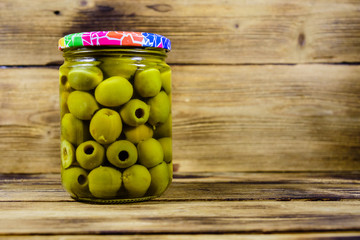 Glass jar with pickled green olives on wooden table
