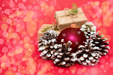 Christmas or New Year composition with a red ball and fir cones. Gift boxes with green twigs on a red background with colorful bokeh.