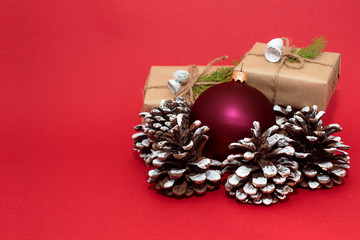 Christmas or New Year composition with a red ball and fir cones. Gift boxes with green sprigs on a red background.