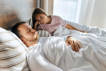 Angry woman can not sleep because of noise, woke up hearing snoring of husband, lying in bed, staring at man, demonstrating irritation, woman tired after sleepless night, tension concent, portrait