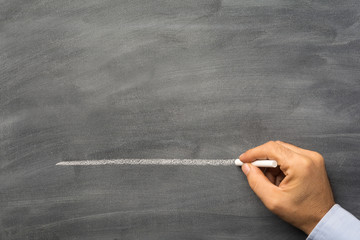 Male hand draws a dash line with chalk on a blank blackboard