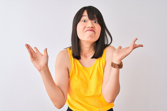 Young beautiful chinese woman wearing yellow t-shirt over isolated white background clueless and confused expression with arms and hands raised. Doubt concept.