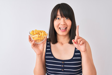 Young beautiful Chinese woman holding bowl with macaroni over isolated white background surprised with an idea or question pointing finger with happy face, number one