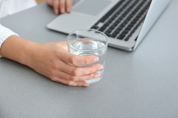 Woman with glass of fresh water and laptop working in office, closeup