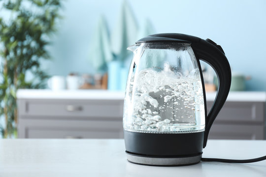 Transparent electric kettle with boiling water on table in kitchen