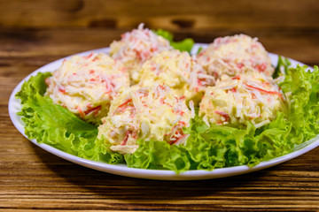 White plate with crab-cheese balls and lettuce leaves on wooden table