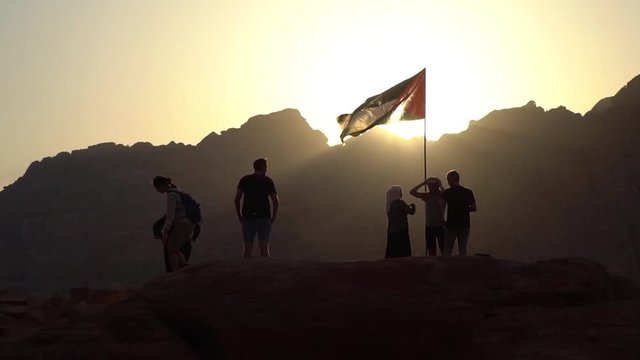 Tourists watching sunset while standing under Jordanian flag, Petra, Jordan