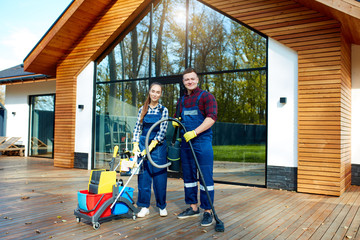 Young caucasian cleaners from cleaning service posing holding detergents, cleaning equipment. Look...