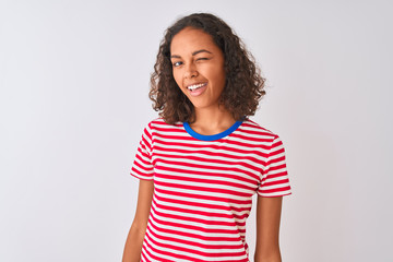 Young brazilian woman wearing red striped t-shirt standing over isolated white background winking...