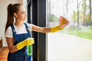 Long haired woman in uniform cleaning panoramic window with spray - obrazy, fototapety, plakaty