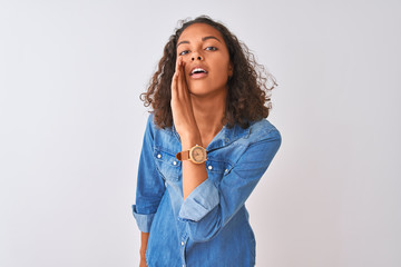 Young brazilian woman wearing denim shirt standing over isolated white background hand on mouth telling secret rumor, whispering malicious talk conversation