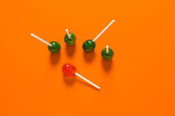 Orange lollipop among green ones on color background. Concept of uniqueness