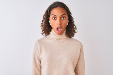 Brazilian woman listening to music using wireless earphones over isolated white background scared...