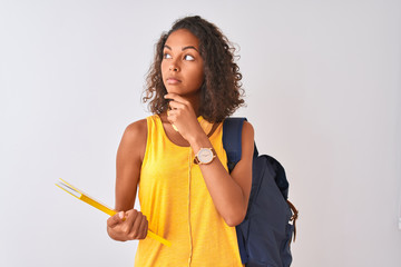 Brazilian student woman wearing backpack holding notebook over isolated white background serious...