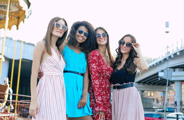 Fototapeta na wymiar Fancy day. A group of four women in sunglasses and multicolored dresses are posing for a joint photo on the urban background.