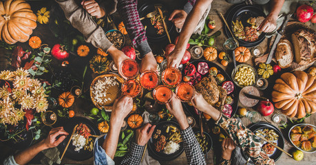 Family celebrating Thanksgiving day. Flat-lay of feasting peoples hands clinking glasses with rose wine over Friendsgiving table with traditional Fall food, roasted turkey, pumpkin pie, top view - 300201424