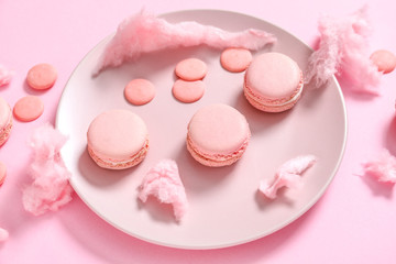 Plate with tasty macarons and sweets on color background