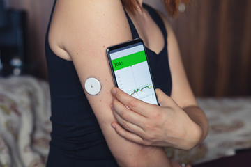 Woman checking glucose level with a modern technology remote sensor and mobile phone, without...