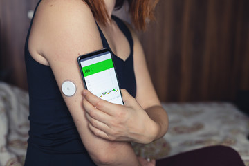 Woman checking glucose level with a modern technology remote sensor and mobile phone, without blood. Diabetes treatment.