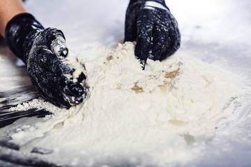 baker's hands in black gloves knead the dough.