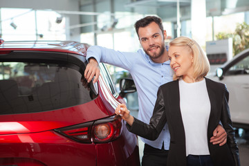 Happy couple hugging near their new car at the dealership. Love, travel, consumerism concept