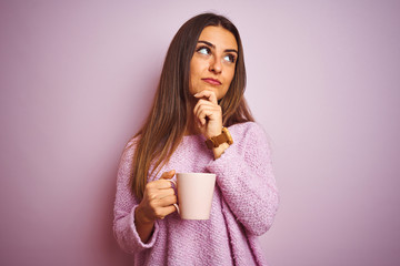 Young beautiful woman drinking cup of coffee standing over isolated pink background serious face...
