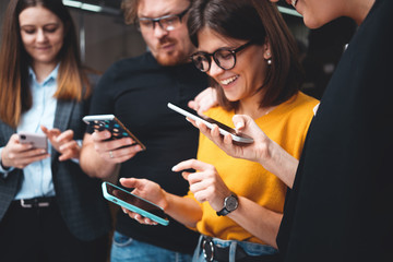Adult group of happy hipsters stand in line and using in hands modern smartphone. Positive business team hold in hand digital phone