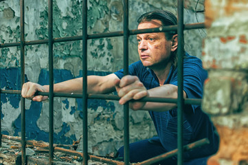 A depressed man holds his hands on the prison bars. Prisoner for the crime. Poor conditions....
