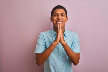 Young handsome arab man wearing blue shirt standing over isolated pink background begging and...