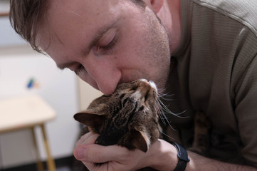 handsome man holding and kissing cheek adorable tabby stripped cat at home