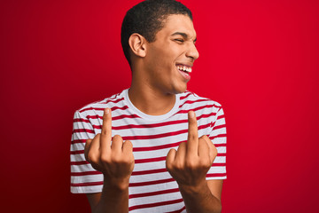 Young handsome arab man wearing striped t-shirt over isolated red background Showing middle finger...