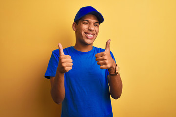 Young handsome arab delivery man standing over isolated yellow background success sign doing positive gesture with hand, thumbs up smiling and happy. Cheerful expression and winner gesture.