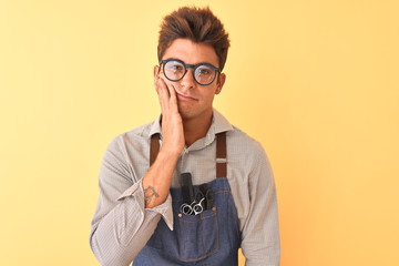 Young handsome hairdresser man wearing apron and glasses over isolated yellow background thinking looking tired and bored with depression problems with crossed arms.