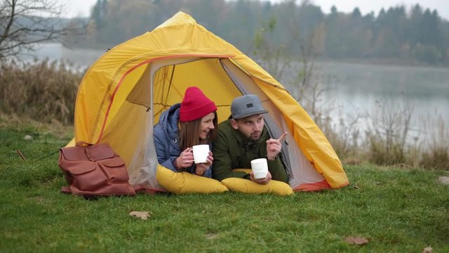 ouple camps in nature with campfire and drinks beverage from vintage white cups