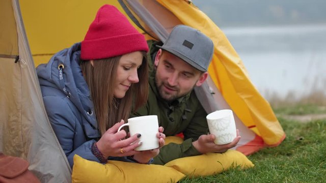 ouple camps in nature with campfire and drinks beverage from vintage white cups