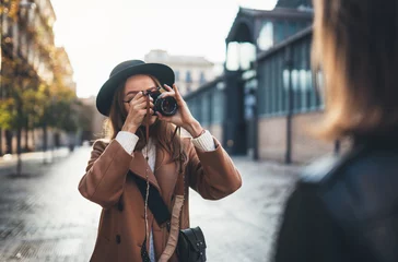 Foto op Plexiglas Outdoor smiling lifestyle portrait of pretty young woman having fun in sun city Europe autumn with camera travel photo of photographer Making pictures in glasses and hat with girlfriends © A_B_C
